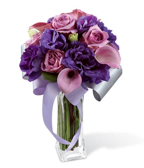 Lavender roses, lavender mini calla lilies, and deep purple double lisianthus in a clear glass flared square vase