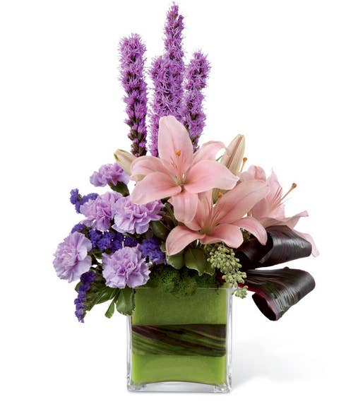 Pink Asiatic lilies, lavender carnations, purple liatris, and purple statice in a glass cubed vase