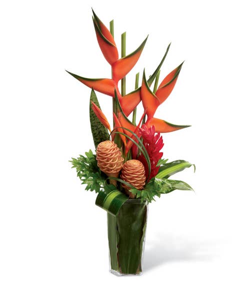 Bright red and green upright heliconia, orange and yellow psitticorum heliconia, shampoo ginger, red ginger and an assortment of tropical leaves and greens in a clear glass tapered square vase