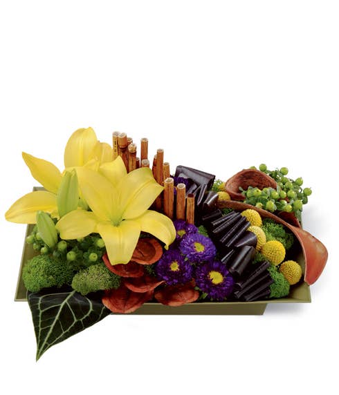 Floral arrangement of yellow asiatic lilies, purple matsumoto asters, green hypericum berries, yellow craspedia, red ti leaves, anthurium leaves, dyed river cane stems, land lotus petals, and elephant ear pods