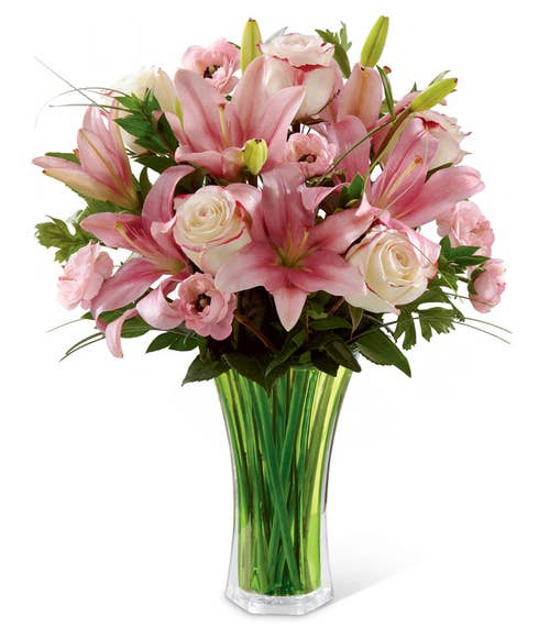Bi-colored pink and white roses, pink ranunculus, pink Asiatic lilies, bear grass & lush greens arranged in a green flared glass vase