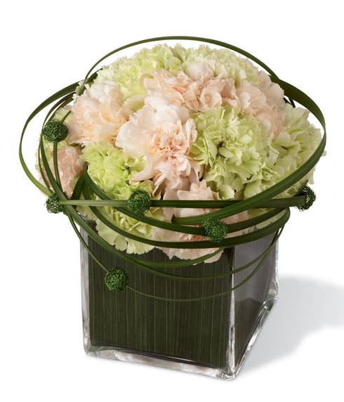 Peach carnations, light green carnations, and lily grass in a clear glass cubed vase
