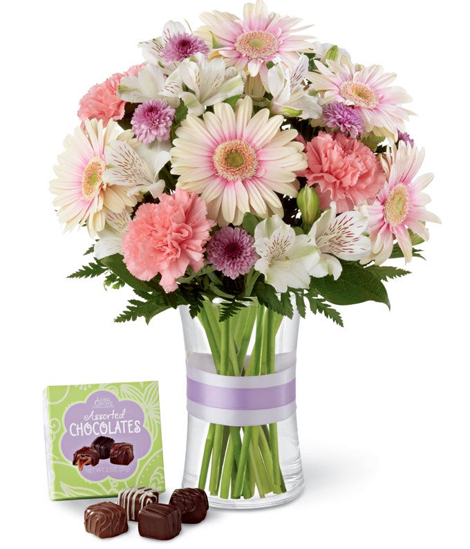 A Bouquet of  Palest White-Pink Gerbera Daisies, Bi-Colored Pink & White Peruvian Lilies, Light-Pink Carnations, Lavender Mums, Alstroemeria in a Keepsake Tell Glass Vase with Lavender Ribbon and Small Box Of Chocolate