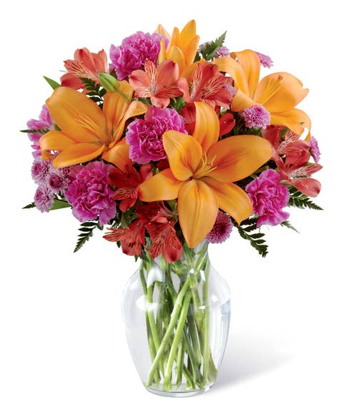 Orange lilies and pink carnations flower bouquet arrangement in a glass vase
