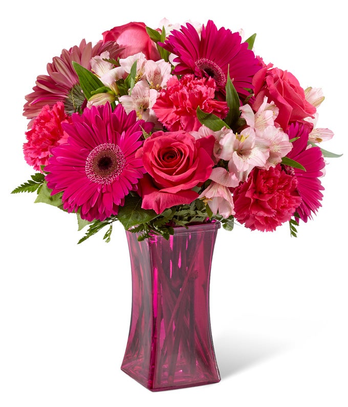 A Bouquet of Fuchsia Gerbera Daisies, Pink Peruvian Lilies, Lavender Roses, Red Spray Roses and Lush Greens in a Berry-colored Glass Vase