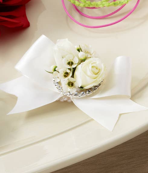 Wristlet with white spray roses and white waxflower brought together with an ivory satin ribbon