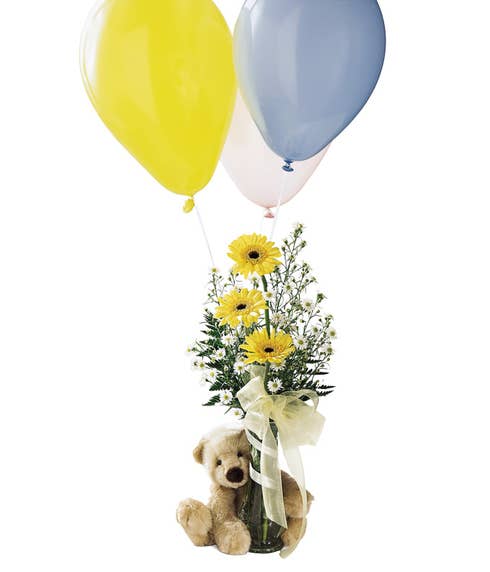 Yellow gerbera daisies are in a vase with a teddy bear and balloon