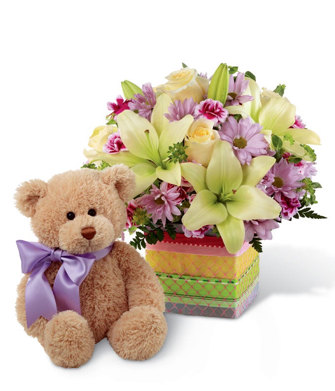 A bouquet of cream roses, white Asiatic lilies, and lavender daisies on a glass cubed vase with a decorative ribbon and 10 inch bear