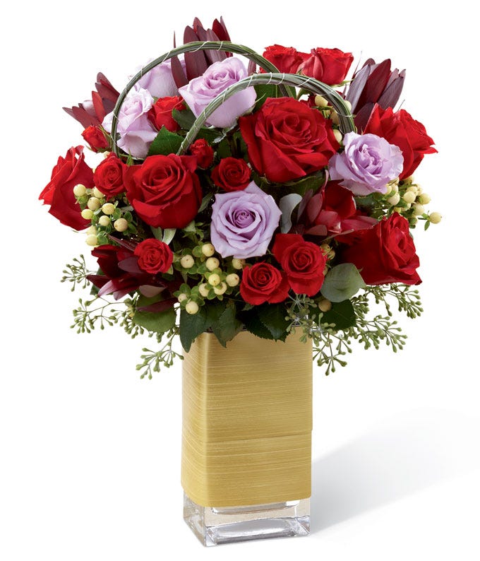 Red roses, lavender roses, red spray roses, white hypericum berries, and lush greens in a clear glass vase