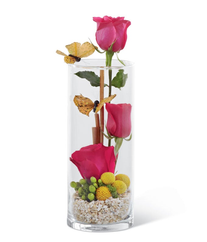 A bouquet of Hot Pink Roses, Green Hypericum Berries, Yellow Craspedia and Natural Stone in a Clear Glass Vase