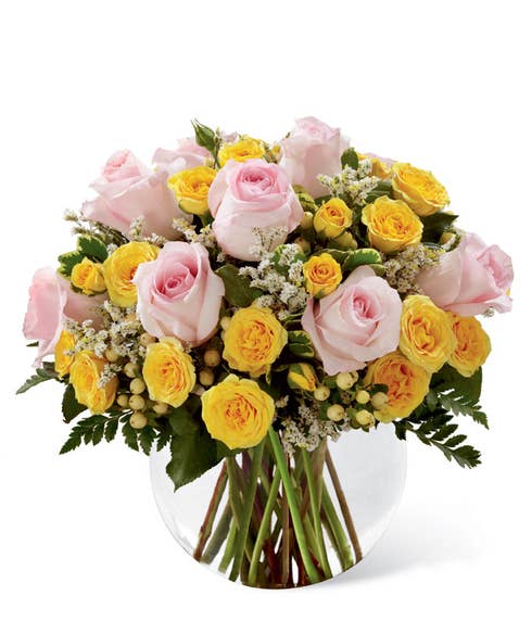 Pink roses, yellow spray roses, white hypericum berries, and white limonium in a clear glass bubble bowl vase