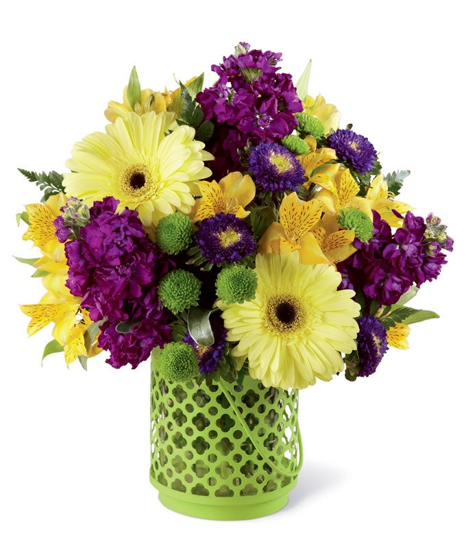 A Bouquet of Yellow Gerbera Daisies, Purple Stock, Yellow Alstroemeria, and Green Button Poms in a Green Lantern Vase