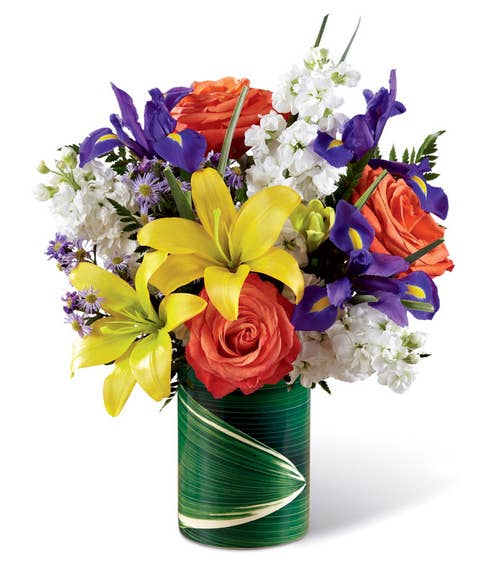 Yellow lily orange rose and white stock flowers bouquet in a leaf wrapped vase