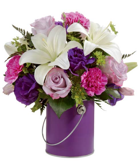 White lilies and lavender roses with pink carnations in a purple paint can vase