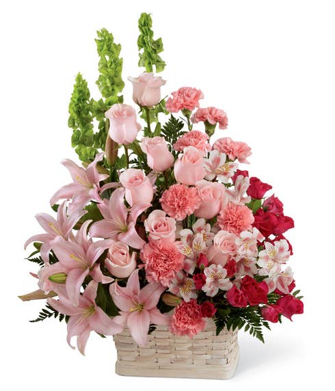 Pink roses, pink lilies and fuchsia carnations in woven basket for delivery