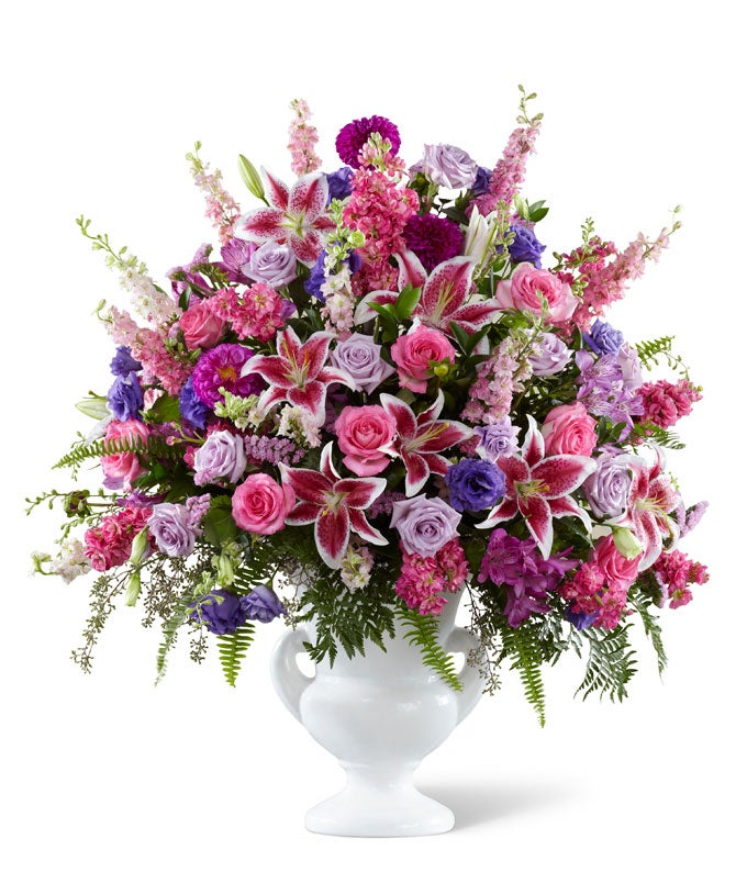 A Bouquet of Dahlias, Lisianthus, Lavender Roses, Hot Pink Roses, Stargazer Lilies and Pink Statice in a  white ceramic urn