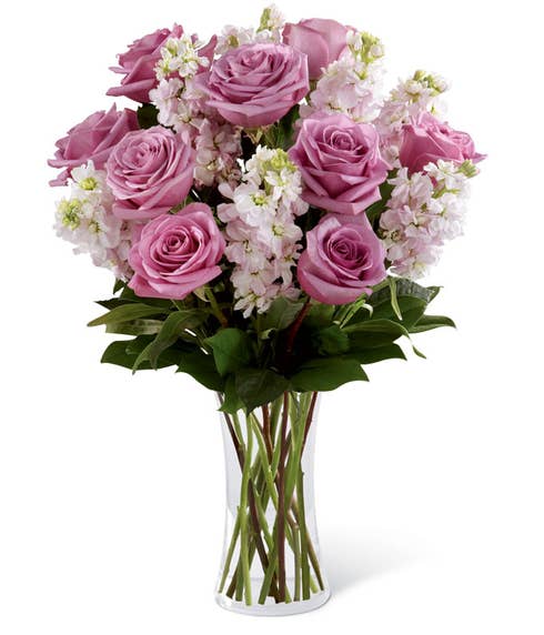 Purple roses, pink flowers and greens in clear vase 