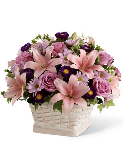 Purple roses, pink lilies and purple daisies in woven basket for a sympathy flowers