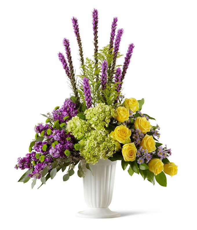 A Bouquet of Yellow Roses, Jade Hydrangea,  Purple Liatris, Violet Stock, Lavender Monte Casinos, and Green Button Pom  in a White Urn