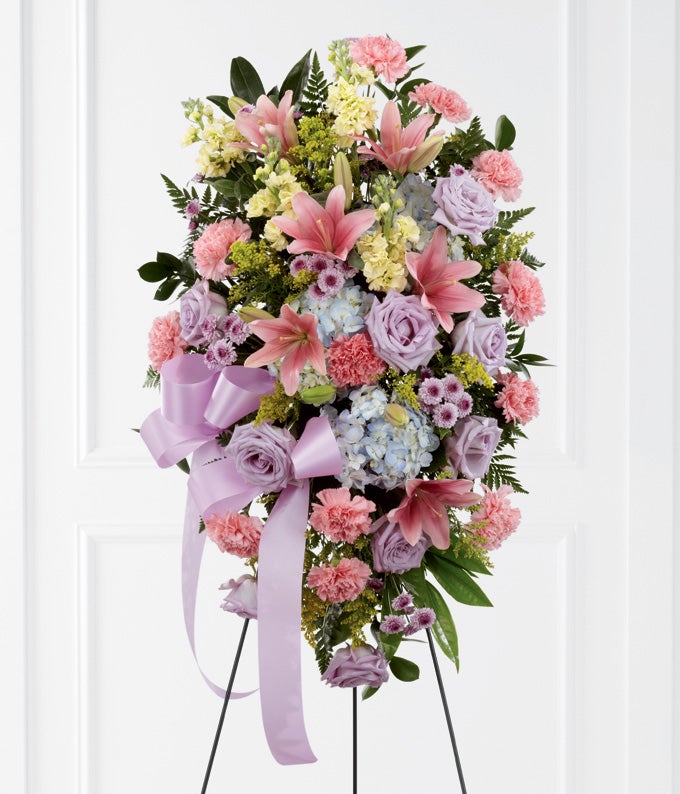 Oval Shape Flower Arrangement Including Lavender Roses, Pink Carnations, Blush Asiatic Lilies, Blue Hydrangea, Solidago, Lavender Button Poms with Beautiful Bow, Stand And Card Included