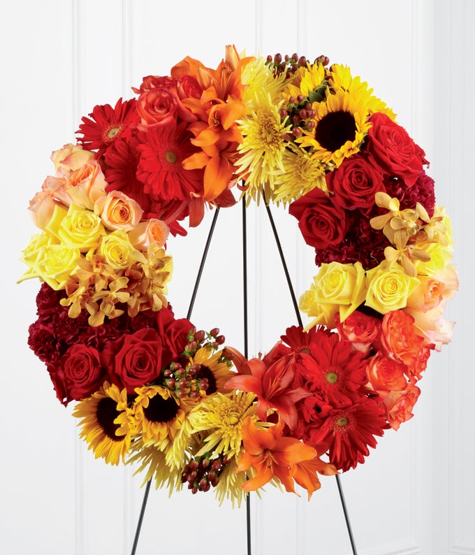  Round Flower arrangement including Yellow Roses, Red Roses, Orange Bi-Color Roses, Gold Mokara Orchids, Yellow Spider Chrysanthemums, Red Gerbera Daisies, Burgundy Carnations, Sunflowers, Orange Asiatic Lilies, and Brown Hypericum Berries