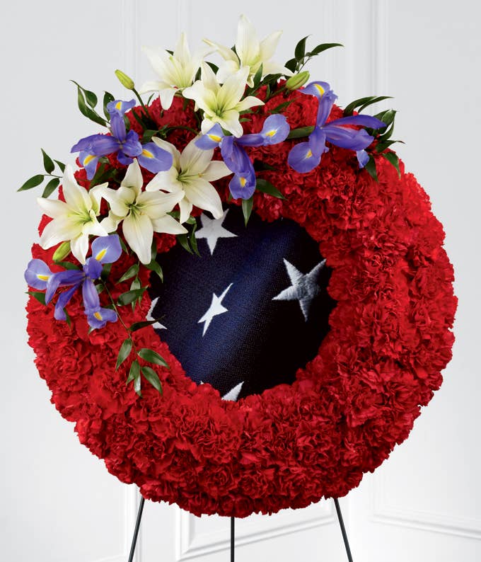 A Round Flower Arrangement of Blue Iris, Red Carnations, and White Asiatic Lilies with America Flag Inspired Fabric, Card Message and Stand Included