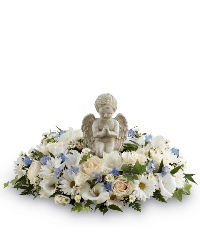 A centerpiece arrangement of White Roses, White Gladiolus, Light Blue Delphinium, White Traditional Daisies, White Monte Casino Asters and Lush Greens with angel statue
