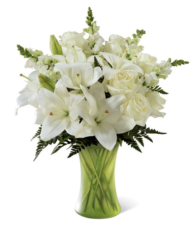 A bouquet of White Roses, Cream Snapdragons and Pearly Asiatic Lilies on a Green Glass Vase