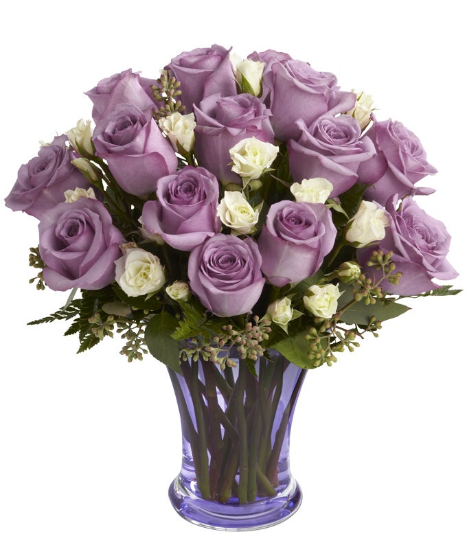 A bouquet of Purple Roses and White Spray Roses in a Colorful Glass Vase