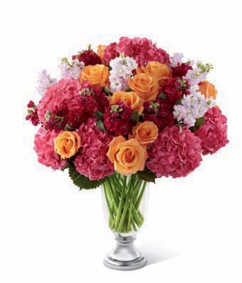 Orange roses, pink hydrangea, hot pink stock, and pale pink stock in a designer glass and metal urn