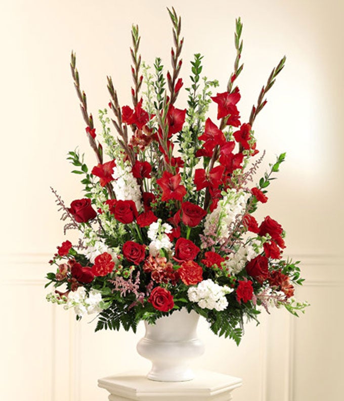 A traditional altar flower arrangement of Red Roses, Crimson Carnations, Larkspur, Pink Astilbe and White Stock in a white vase