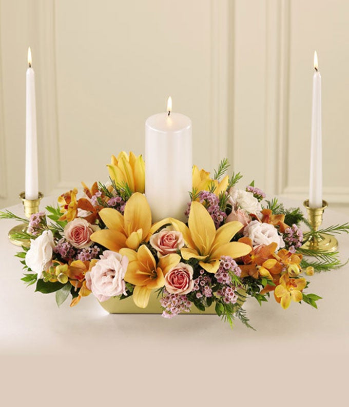 A centerpiece arrangement of Mango Mokara Orchids, Light-Peach Asiatic Lilies, Light-Pink Spray Roses, and Pink Lisia thus in a Keepsake Container with Three Candles Included