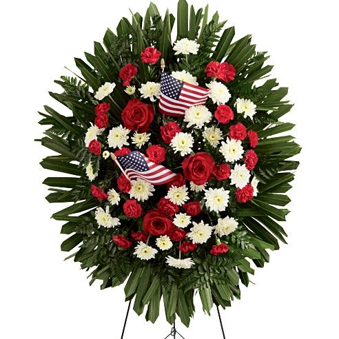 Oval Shaped Flower Centerpiece Including Red Roses, Crimson Mini Carnations, White Chrysanthemums and Lush Greens with Decoration Flags