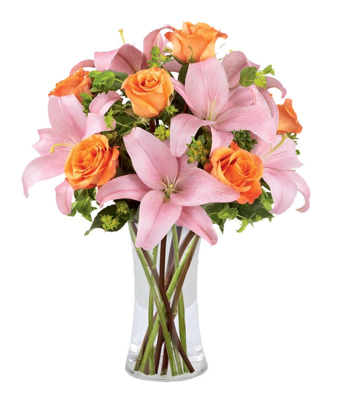 Orange roses and pink asiatic lilies with greens in a clear glass vase