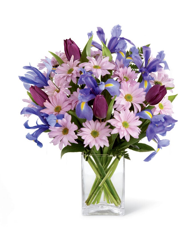 A bouquet of Dark Blue Iris, Purple Tulips, Lavender Daisies and Greenery in a Rectangle Glass Vase