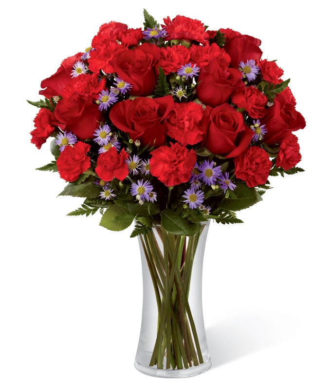 A bouquet of Red Roses, Ruby Mini Carnations, Purple Monte Casino and Seasonal Greens on a glass vase