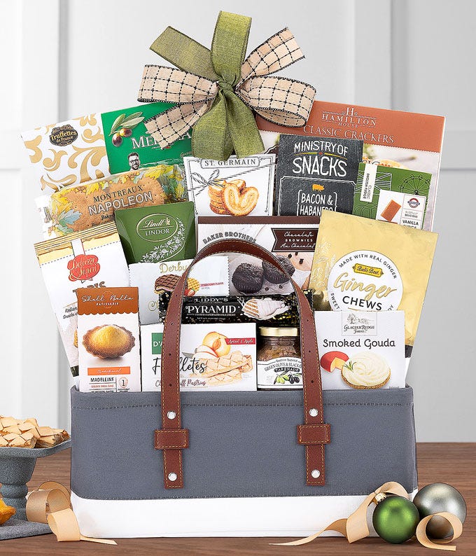 Gift basket in a gray and white tote with a plaid bow, filled with assorted gourmet snacks including crackers, cookies, cheese, chocolates, nut mixes, and ginger chews, surrounded by festive ornaments and ribbon.