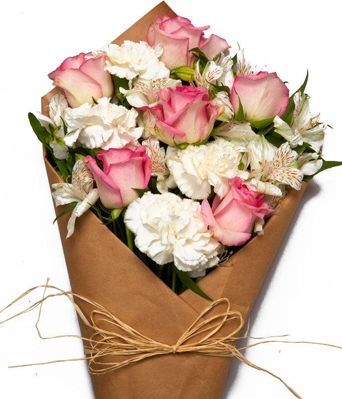 A Bouquet of Pink Roses, White Alstroemeria, White Mini Carnations, and Fresh Greens Wrapped in a Brown Parchment Paper with Twine Tie