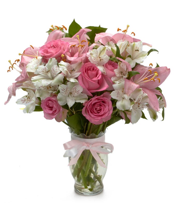 A bouquet of Pink Roses, Light-Pink Lilies and White Alstroemeria in a clear glass vase with a pink ribbon