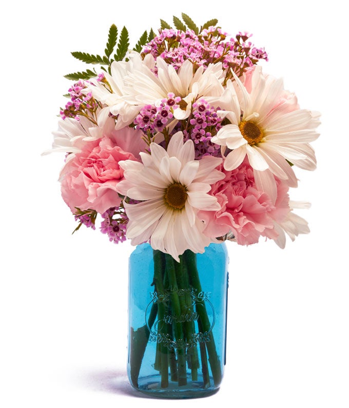 A Bouquet of White Daisies, Pink Carnations, Blush Waxflower, and Fresh Greens in a Blue Mason Jar Vase