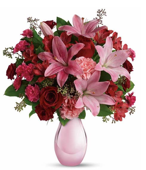 Pink lily, pink carnations, and red roses bouquet in a pink glass vase
