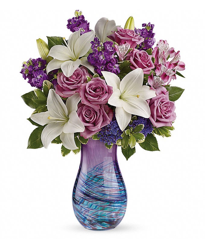 A Bouquet of  Lavender Roses, Purple Alstroemeria, White Asiatic Lilies, Purple Seafoam Statice and Lush Greens in a Blown Glass Vase