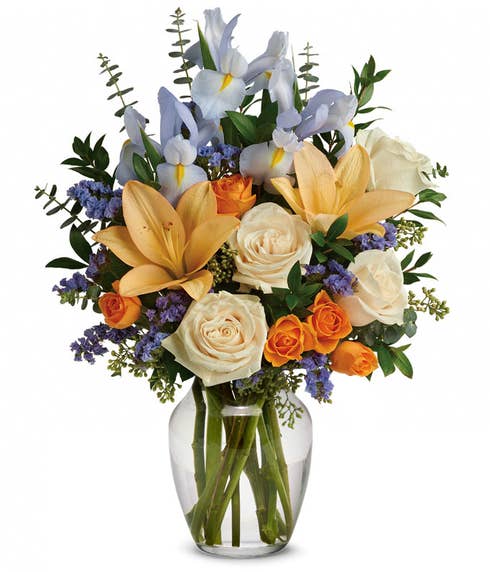 Spring bouquet of cream roses, light blue iris, peach lilies and orange spray roses