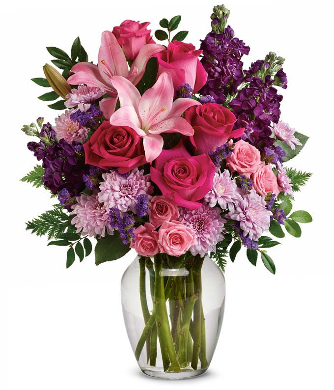 A bouquet of Hot Pink Roses, Pink Spray Roses, Light Pink Asiatic Lilies, Purple Stock, Lavender Cushion Spray Chrysanthemums, Purple Sinuata Statice, Huckleberry and Leatherleaf Fern in a Clear Glass Vase