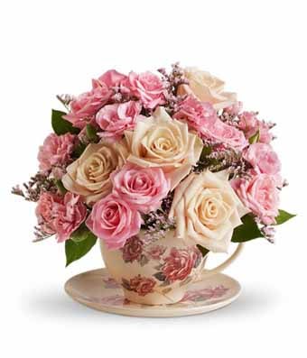 A bouquet of pink roses, hot pink mini carnations, fresh greens and blush Peruvian lilies on a clear glass vase