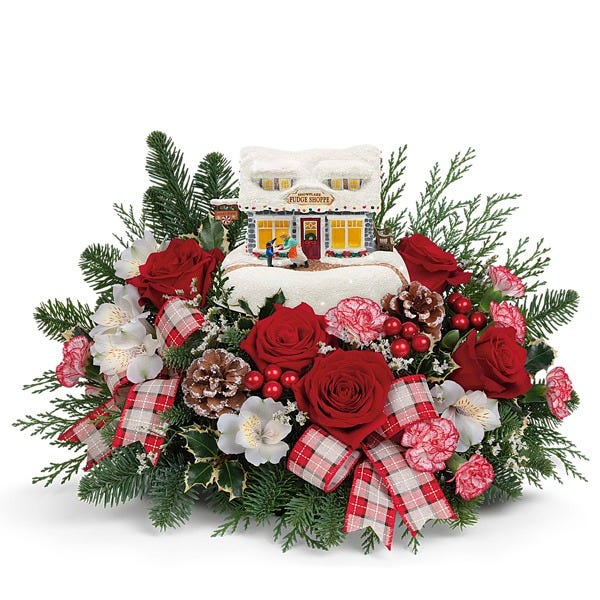 Centerpiece of red roses, white flowers, berries, pinecones, and ribbon, with a Thomas Kinkade Sweet Shoppe keepsake house.
