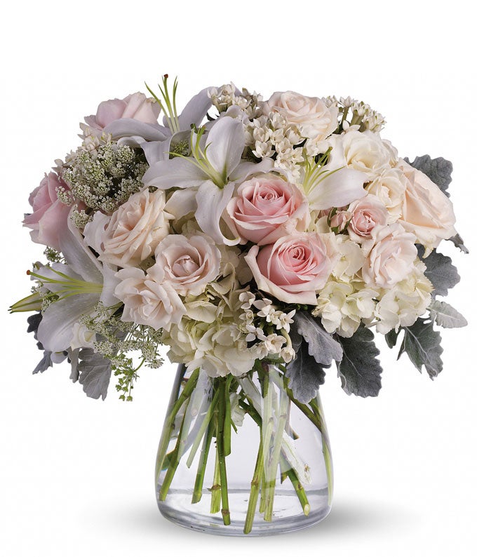 A bouquet of White Roses, Cream Roses, Pink Roses, White Hydrangea, and White Queen Annes Lace in a Clear Glass Vase