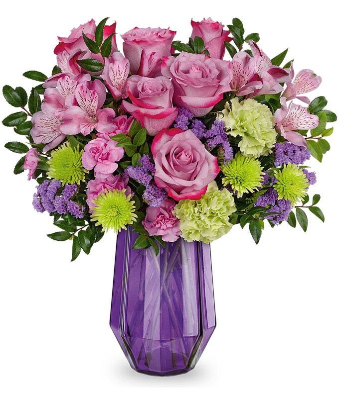 Tall, round, bouquet of purple and green flowers in a tall geometric purple vase