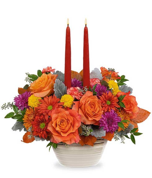 Orange Roses & Carnations, lavender cushion spray chrysanthemums, dark bronze daisy spray chrysanthemums, brown copper beech, dusty miller, seeded eucalyptus, huckleberry in a beige rustic bowl with two burgundy taper candles