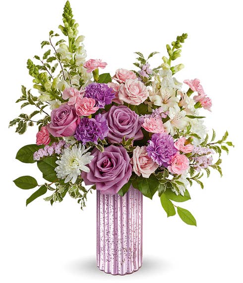 A Mother's Day arrangement featuring lavender roses, pink spray roses, purple carnations, pink miniature carnations, white snapdragons, white cushion spray chrysanthemums, floral greens, all arranged in a metallic lavender vase, with space 